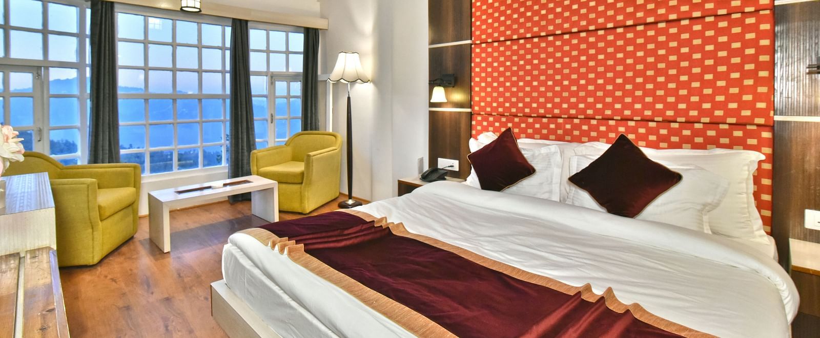 A bedroom with a seating area by the window, offering a mountain view at DLS Hillcrest Resort, Shimla.